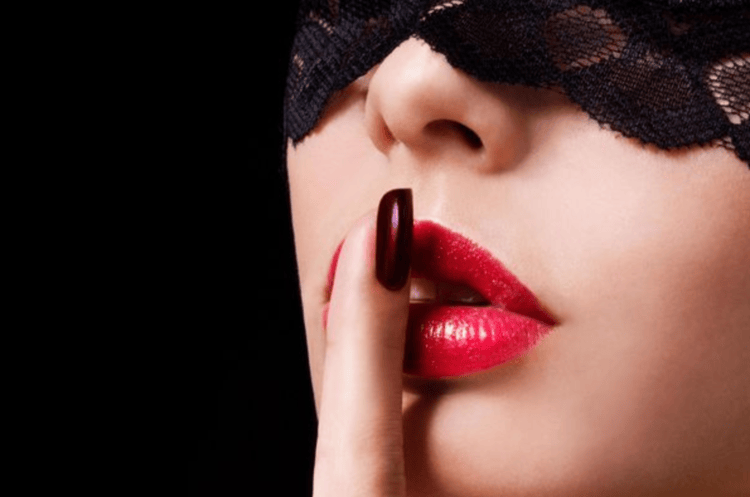 masked woman doing hush sign for fetish massage